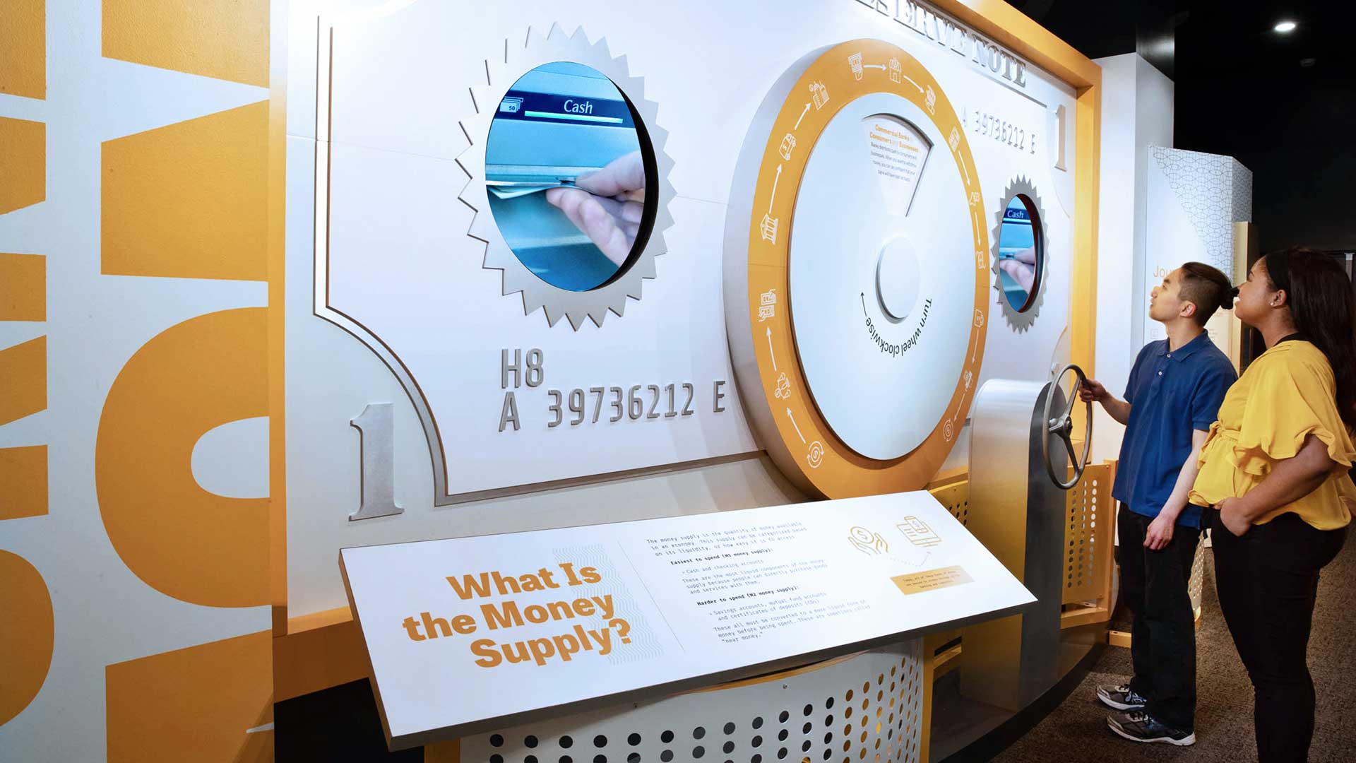 Two people stand in front of an interactive exhibit with a wheel that moves the display in a circle.
